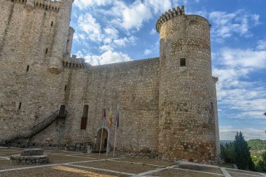 İkonik Castillo de Torija, sağlam taş duvarlar ve silindirik kuleler, canlı mavi bir gökyüzüne karşı dimdik ayakta duruyor ve yeşilliklerle çevrili..