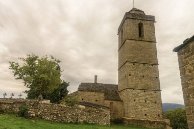 Ağaçlarla çevrili, uzun bir kulesi ve kırsal mimarisi olan antik taş kilise..