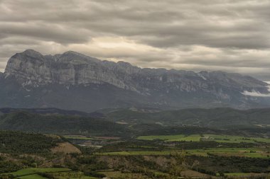 Tarlaların, küçük bir kasabanın ve bulutlu bir gökyüzünün altında görkemli dağların bulunduğu güzel bir vadi manzarası..