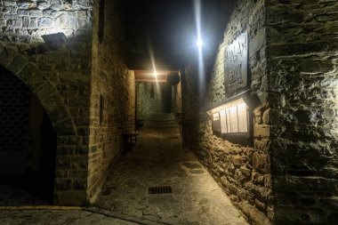 Geceleri sıcacık sokak lambalarıyla aydınlatılmış, taşlarla döşenmiş sessiz bir sokak. Sıcak bir köy restoranına çıkıyor..