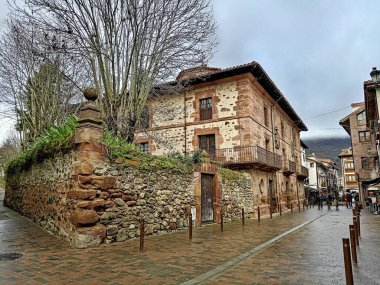 Dairesel pencereleri ve ıslak sokakta taş bahçe duvarları olan eski asil bir ev.