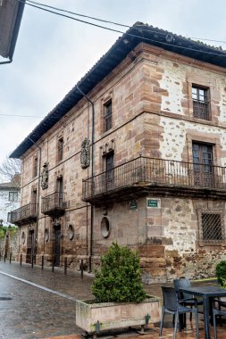 Köy köşesinde oyulmuş armalı taş ev ve dövülmüş demir balkonlar.