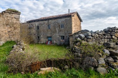 Sakin bir köyde eski duvarlar ve yeşilliklerle çevrili yıpranmış taş bir ev.