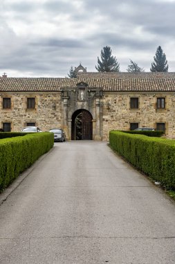 Merkezi kemerli kapılı ve girişe giden manikürlü çitleri olan bir manastır cephesi..
