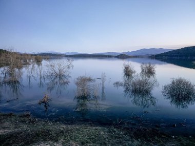 Aguilar de Campoo, Palencia, İspanya 'da dağlarla ve dramatik bulutlarla dolu huzurlu rezervuar manzarası.