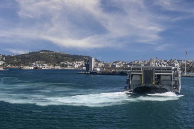 Mavi kargo gemisi ve römorkör arka planda tepelerle Ceuta limanında geziniyor..