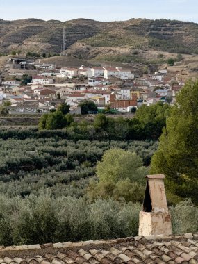 Kurak arazide zeytin tarlalarına ve köye bakan geleneksel taş bina.