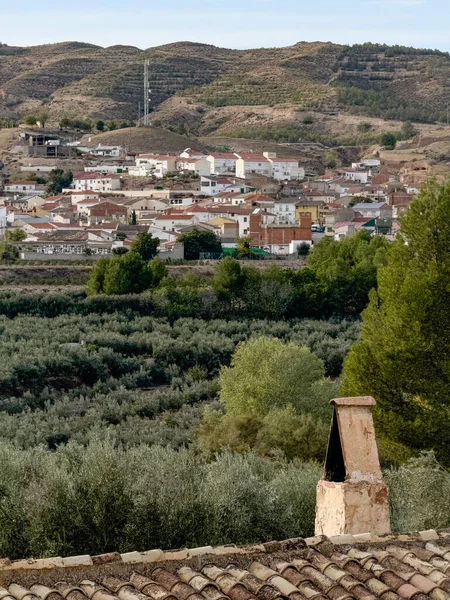 Kurak arazide zeytin tarlalarına ve köye bakan geleneksel taş bina.