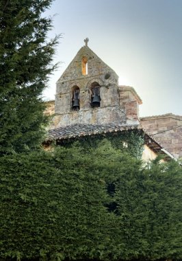 Tepeler ve açık mavi gökyüzünün altındaki kırsal duvarlarla çevrili antik taş kilise.