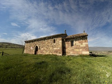 Parlak mavi gökyüzünün altındaki yeşil bir çayırda antik taş inziva yeri.