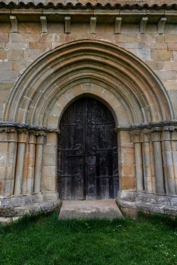 Palencia 'daki Santa Eulalia inzivasında yarı dairesel kemerli ve ahşap kapılı Romen taş portalı..