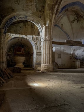 Terk edilmiş kilise içinde taş sütunlar, kemerler ve vaftiz fontu var..