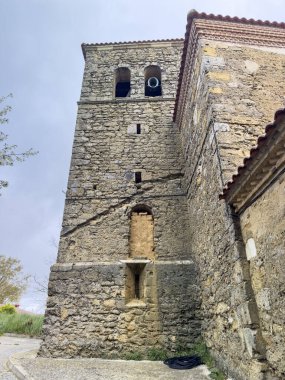 Çan kulesi ve kemerli verandalı, Quintanilla de Osona 'daki ağaçlar ve çitlerle çevrili taş kilise.