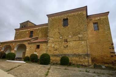 Çan kulesi ve kemerli verandalı, Quintanilla de Osona 'daki ağaçlar ve çitlerle çevrili taş kilise.