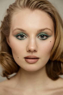 Güzel stüdyo portresi. Mutlu, iyimser, neşeli, güzel, ciltli, makyajlı, saç stili olan güzel bir kadın. Gri duvar arkasında çıplak poz veriyor.