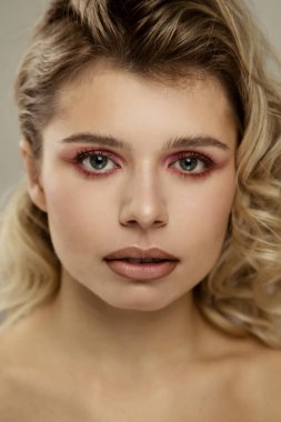 Güzel stüdyo portresi. Mutlu, iyimser, neşeli, güzel, ciltli, makyajlı, saç stili olan güzel bir kadın. Gri duvar arkasında çıplak poz veriyor.