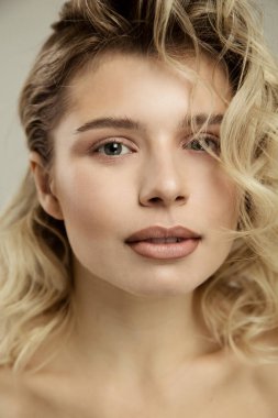 Güzel stüdyo portresi. Mutlu, iyimser, neşeli, güzel, ciltli, makyajlı, saç stili olan güzel bir kadın. Gri duvar arkasında çıplak poz veriyor.