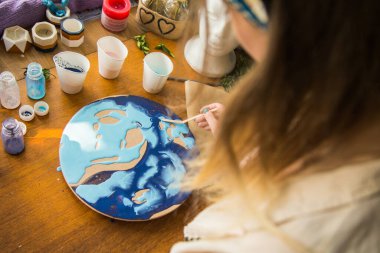 Kadın sanatçı, mermer efektli soyut akışkan sanat eserleri üzerinde çalışır, güzel genç kadın ressamın portresini yakından çekerek ahşap bir masa üzerinde yaratıcı çalışma alanında sanat eserleri yaratır.