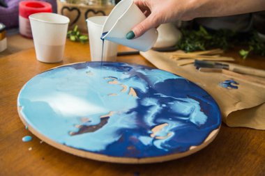 Kadın sanatçı, mermer efektli soyut akışkan sanat eserleri üzerinde çalışır, güzel genç kadın ressamın portresini yakından çekerek ahşap bir masa üzerinde yaratıcı çalışma alanında sanat eserleri yaratır.