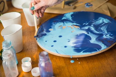 Kadın sanatçı, mermer efektli soyut akışkan sanat eserleri üzerinde çalışır, güzel genç kadın ressamın portresini yakından çekerek ahşap bir masa üzerinde yaratıcı çalışma alanında sanat eserleri yaratır.