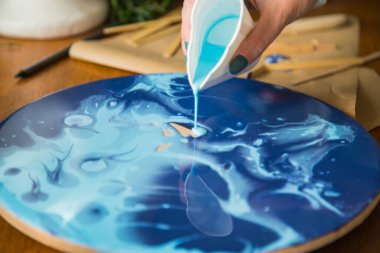 Kadın sanatçı, mermer efektli soyut akışkan sanat eserleri üzerinde çalışır, güzel genç kadın ressamın portresini yakından çekerek ahşap bir masa üzerinde yaratıcı çalışma alanında sanat eserleri yaratır.