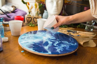 Kadın sanatçı, mermer efektli soyut akışkan sanat eserleri üzerinde çalışır, güzel genç kadın ressamın portresini yakından çekerek ahşap bir masa üzerinde yaratıcı çalışma alanında sanat eserleri yaratır.