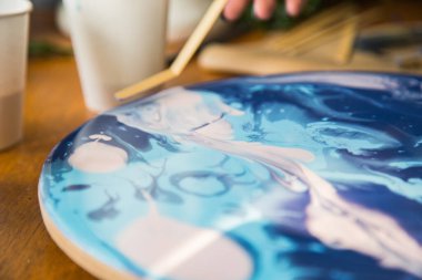 Kadın sanatçı, mermer efektli soyut akışkan sanat eserleri üzerinde çalışır, güzel genç kadın ressamın portresini yakından çekerek ahşap bir masa üzerinde yaratıcı çalışma alanında sanat eserleri yaratır.