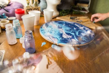 Kadın sanatçı, mermer efektli soyut akışkan sanat eserleri üzerinde çalışır, güzel genç kadın ressamın portresini yakından çekerek ahşap bir masa üzerinde yaratıcı çalışma alanında sanat eserleri yaratır.