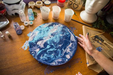 Kadın sanatçı, mermer efektli soyut akışkan sanat eserleri üzerinde çalışır, güzel genç kadın ressamın portresini yakından çekerek ahşap bir masa üzerinde yaratıcı çalışma alanında sanat eserleri yaratır.