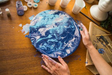 Kadın sanatçı, mermer efektli soyut akışkan sanat eserleri üzerinde çalışır, güzel genç kadın ressamın portresini yakından çekerek ahşap bir masa üzerinde yaratıcı çalışma alanında sanat eserleri yaratır.