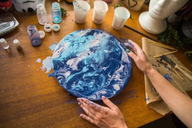 Kadın sanatçı, mermer efektli soyut akışkan sanat eserleri üzerinde çalışır, güzel genç kadın ressamın portresini yakından çekerek ahşap bir masa üzerinde yaratıcı çalışma alanında sanat eserleri yaratır.