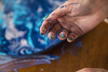 Kadın sanatçı, mermer efektli soyut akışkan sanat eserleri üzerinde çalışır, güzel genç kadın ressamın portresini yakından çekerek ahşap bir masa üzerinde yaratıcı çalışma alanında sanat eserleri yaratır.