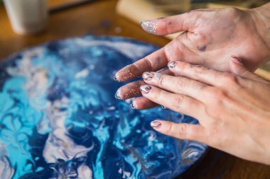 Kadın sanatçı, mermer efektli soyut akışkan sanat eserleri üzerinde çalışır, güzel genç kadın ressamın portresini yakından çekerek ahşap bir masa üzerinde yaratıcı çalışma alanında sanat eserleri yaratır.