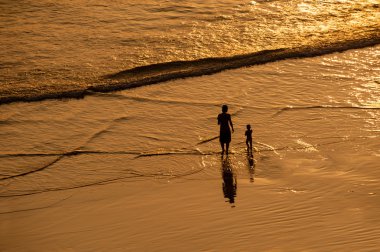 Kadın ve çocuk gün batımında sahilde.