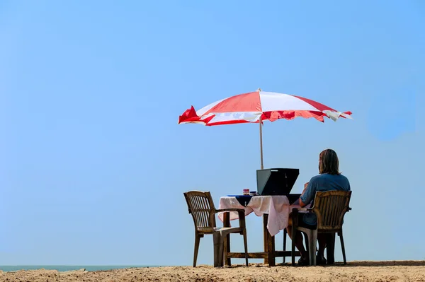 Мужчина сидит за столом на пляже — стоковое фото