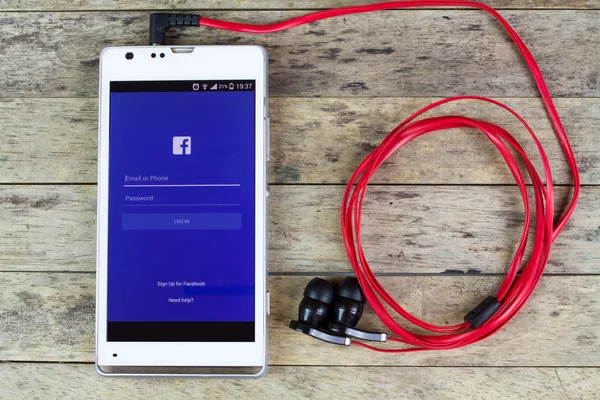 Πώμα Kan, Ταϊλάνδη - 02 Σεπτεμβρίου 2015: χρησιμοποιώντας το facebook από το έξυπνο τηλέφωνο με ακουστικά, facebook ρεύμα μουσική — Φωτογραφία Αρχείου