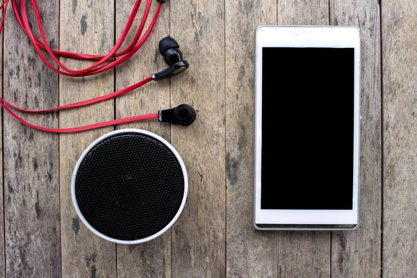 Celular e alto-falante Bluetooth e fone de ouvido em fundo de madeira, conjunto de escuta Fotografia De Stock