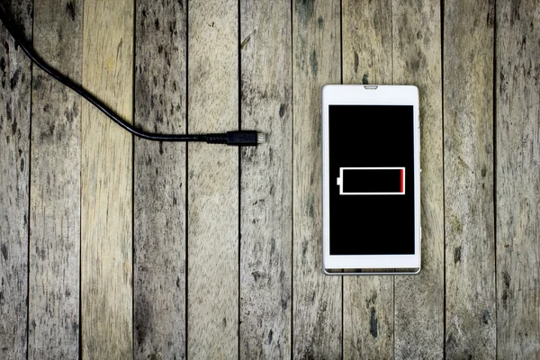 Teléfono inteligente necesidad de cargar una batería en tablón de madera, vista superior Imagen de archivo