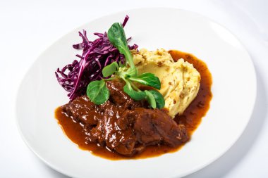 Veal cheeks in gravy with potatoes and cabbage, decorated herbs