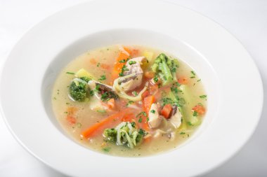 Light fish soup with vegetables and broccoli in white plate.