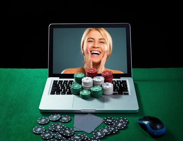 Casino chips and cards on keyboard notebook at green table.