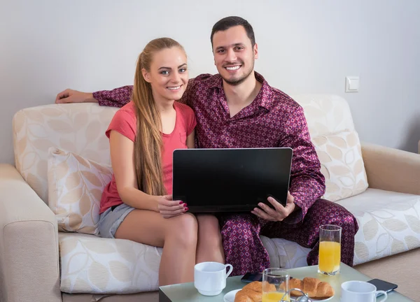 Linda pareja joven desayunando, frente a la computadora portátil — Foto de Stock