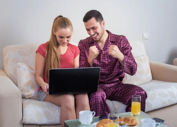 Linda pareja joven desayunando, frente a la computadora portátil — Foto de Stock