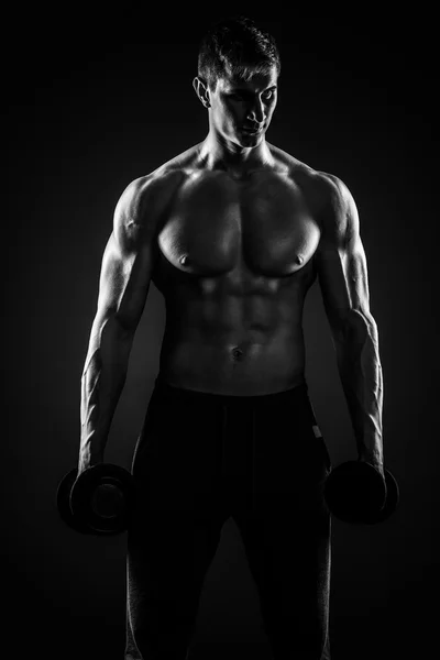 Uomo muscolare mostrando corpo perfetto con manubri su dorso nero — Foto Stock