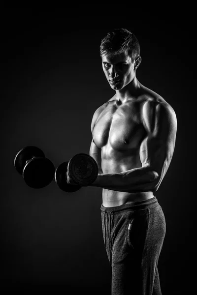 Handsome man showing perfect body with dumbbells on black backgr — Stok fotoğraf