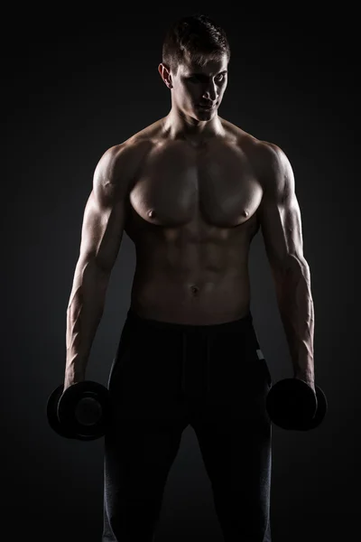 Homem muscular mostrando corpo perfeito com halteres em fundo preto — Fotografia de Stock