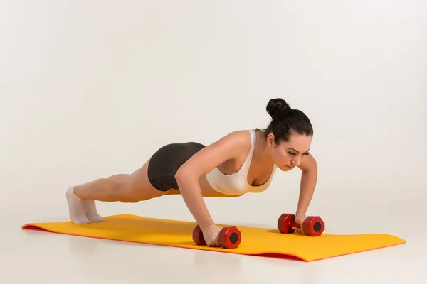 Sterke jonge vrouw doet push ups oefening met halters. — Stockfoto