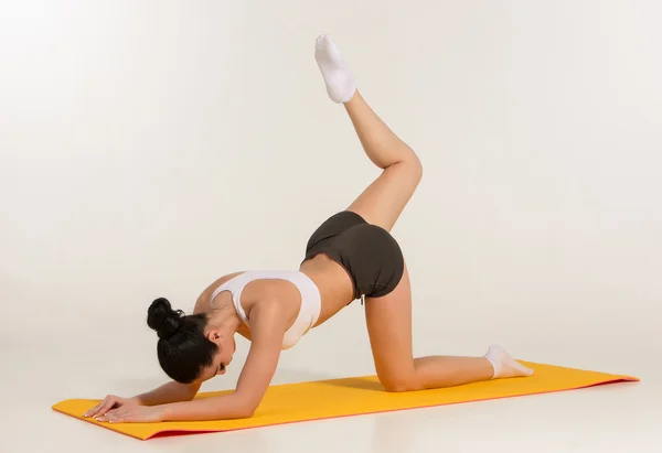 Mujer atractiva haciendo ejercicios. Morena cuerpo en forma en estera de yoga — Foto de Stock