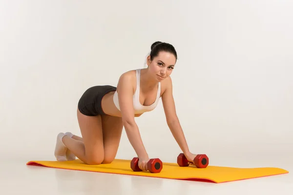 Sterke jonge vrouw doet push ups oefening met halters. — Stockfoto