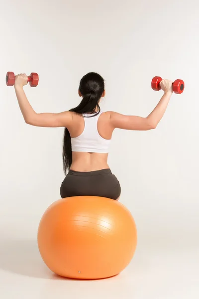 Jonge Sportvrouw doen fitness oefening met halters op pilates bal — Stockfoto